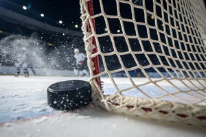 Eishockey-Puck am Torpfosten: Nahaufnahme auf dem Eis mit Tornetz und Eisspray – Hockeyweb.de